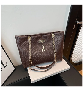 Detail of dark brown woven tote bag featuring a gold deer charm and chain strap