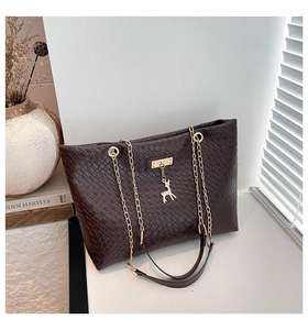 Detail of dark brown tote bag with woven texture, gold chain strap and deer charm