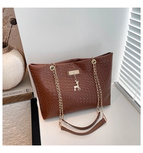 Detail of dark brown woven tote bag featuring a gold chain strap and deer pendant