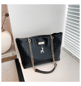 Detail of black woven texture tote bag with gold deer charm and chain strap