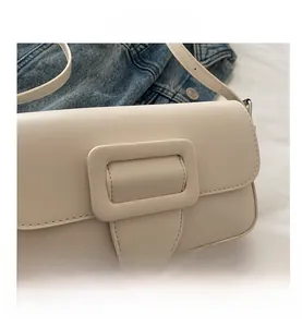 Detail of a creamy beige baguette bag with a large rectangular buckle on denim background