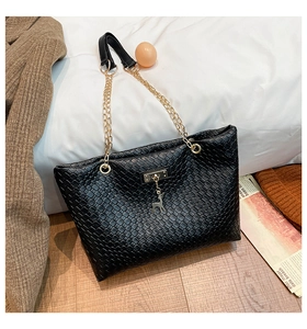 Detail of black woven leather tote bag with golden chain and deer pendant charm