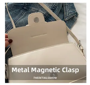 Close-up of the magnetic metal snap closure on a cream-white leather flap shoulder bag