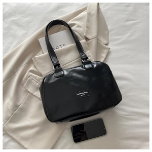Close-up of black waxed leather texture and metal logo plaque on a large tote bag