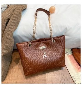 Close-up of brown woven tote bag with gold deer charm and mixed chain strap detail