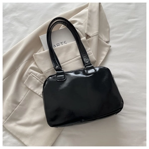 Detail of black glossy leather handbag placed on a beige blazer and art books