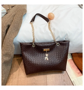 Close-up of brown woven bucket bag featuring gold deer pendant and chain handle