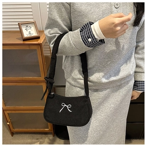 Detail of black corduroy shoulder bag with embroidered white bow on the center