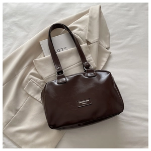Detailed close-up of dark brown oil wax leather handbag on beige blazer fabric