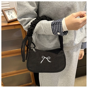 Detail of black corduroy handbag featuring white bow embroidery and ruffled handle