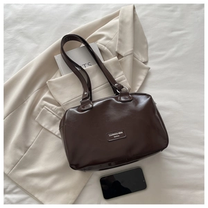 Detail of dark coffee oil-wax leather shoulder bag with a logo plate on a white bed sheet