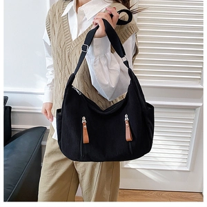 Detail of black corduroy dumpling bag with adjustable wide strap and side zip pockets
