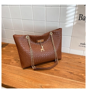 Close-up of dark brown woven tote with golden deer charm and metallic chain strap