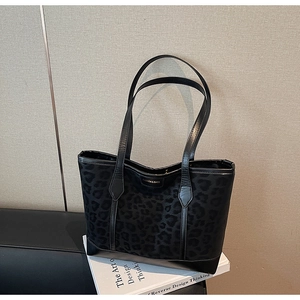 Détail du sac cabas léopard noir avec anses en cuir posé sur des livres blancs