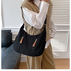 Detail of black corduroy dumpling bag with metal zipper pockets and leather pull tabs