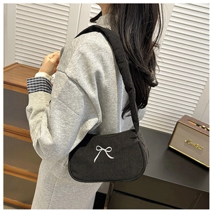 Detail of black corduroy shoulder bag featuring an elegant white bow embroidery