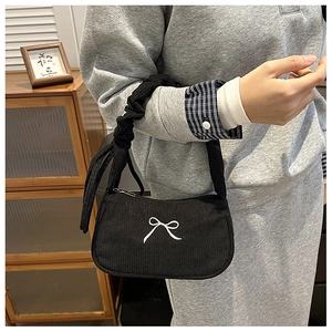 Detail of black corduroy baguette bag with white bow embroidery and pleated handle