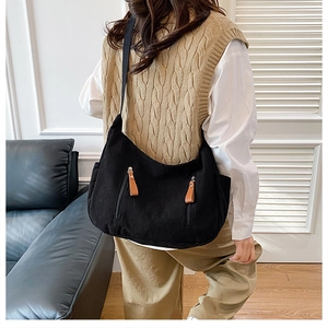 Detail view of black corduroy shoulder bag with front zippers and brown leather pulls