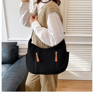 Detail of black corduroy hobo bag with dual vertical zipper pockets and brown leather pulls