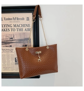 Detail of woven brown tote bag with gold deer pendant and metal chain strap