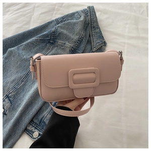 Detail view of pink flap bag with square buckle and adjustable strap on denim background