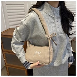 Close-up of khaki corduroy shoulder bag featuring white bow embroidery and ribbon strap