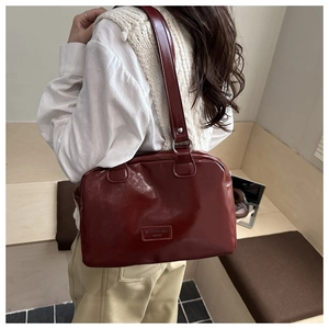 Detail of dark red glossy oil wax leather tote bag with metallic brand plate on shoulder