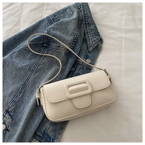 Detail of a minimalist cream white baguette bag placed on a blue denim jacket