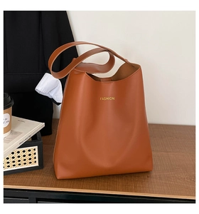 Close-up of caramel faux leather tote bag with gold fashion lettering on wood surface