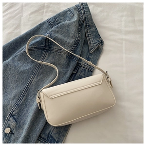 Detailed view of a cream leather baguette bag with flap closure on a denim jacket