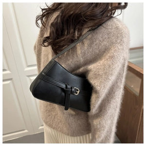 Close-up of a black matte leather baguette bag styled with a brown sweater and white skirt