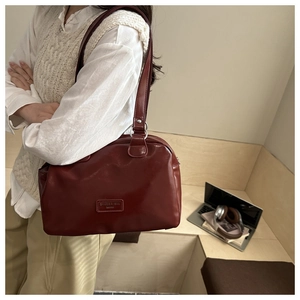 Detail of burgundy wax leather shoulder bag featuring a vintage logo patch and silver rings