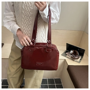 Macro view of dark red Boston bag showing polished faux leather texture and silver rings