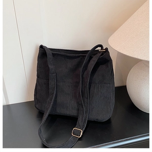 Close-up of black corduroy tote bag featuring vertical stripes and golden metal buckles