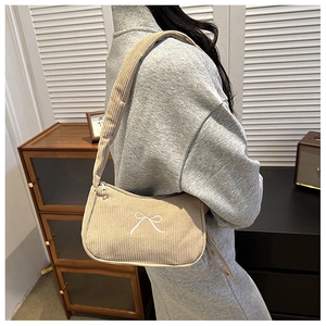 Detail of beige corduroy shoulder bag featuring white embroidered bow and soft texture