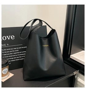 Detail of minimalist black bucket bag with gold 'FASHION' text and wide shoulder strap