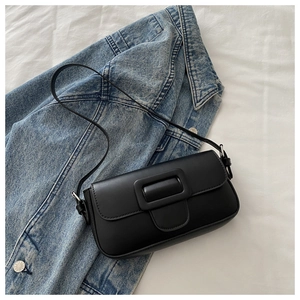 Detail of black faux leather baguette bag with large buckle on a denim jacket
