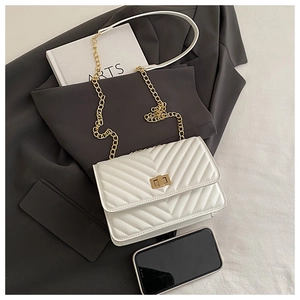 White quilted flap bag with V-stitch design and gold chain strap on grey blazer