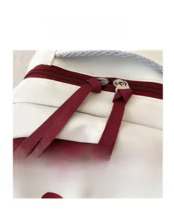 Close-up of double red zippers and durable cream fabric on high-capacity backpack