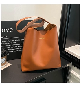 Detailed view of brown leather tote bag featuring gold fashion typography print on surface