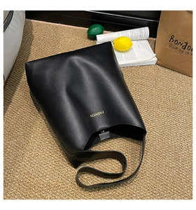 Top view of a minimalist black leather tote bag with gold lettering on a woven rug