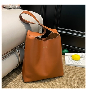 Detailed view of caramel brown leather tote bag with gold FASHION text on a beige rug