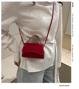 Close-up of a red patent leather mini bag worn with white top and denim jeans