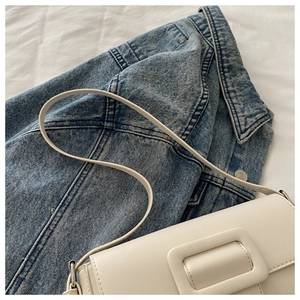 Detail of white satchel bag with square buckle on denim jacket background for fashion