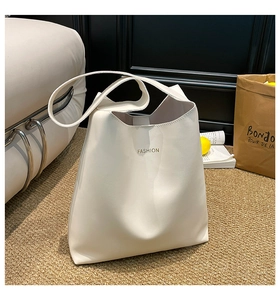 Detailed view of cream-colored tote bag with gold fashion lettering and wide shoulder strap