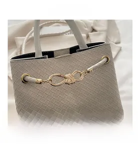 Detail of cream woven tote bag featuring a decorative gold knot buckle and fine texture