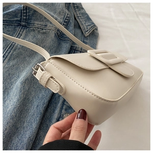 Detail of a minimalist cream PU leather crossbody bag on blue denim jacket background