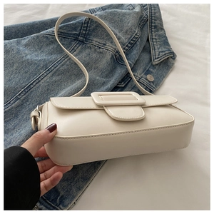 Close-up of cream PU leather baguette bag with large square buckle on denim fabric