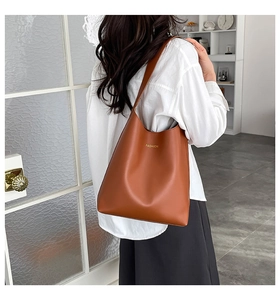 Detail of a brown PU leather tote bag with gold FASHION text being worn by a model