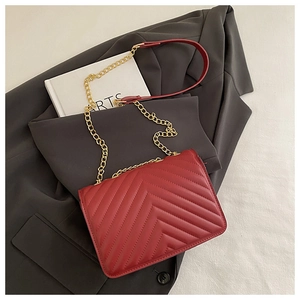 Detail of red quilted crossbody bag with gold chain strap on a professional suit jacket
